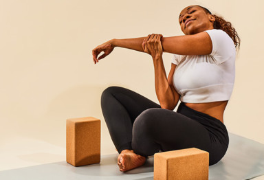 an african american woman stretches her arms on a yoga mat with yoga blocks next to her