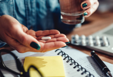 Woman holding pill in hand at desk