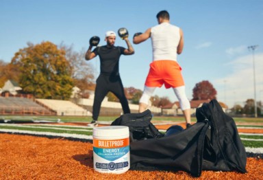 Two men boxing with a gym bag and tub of collagen in the foreground