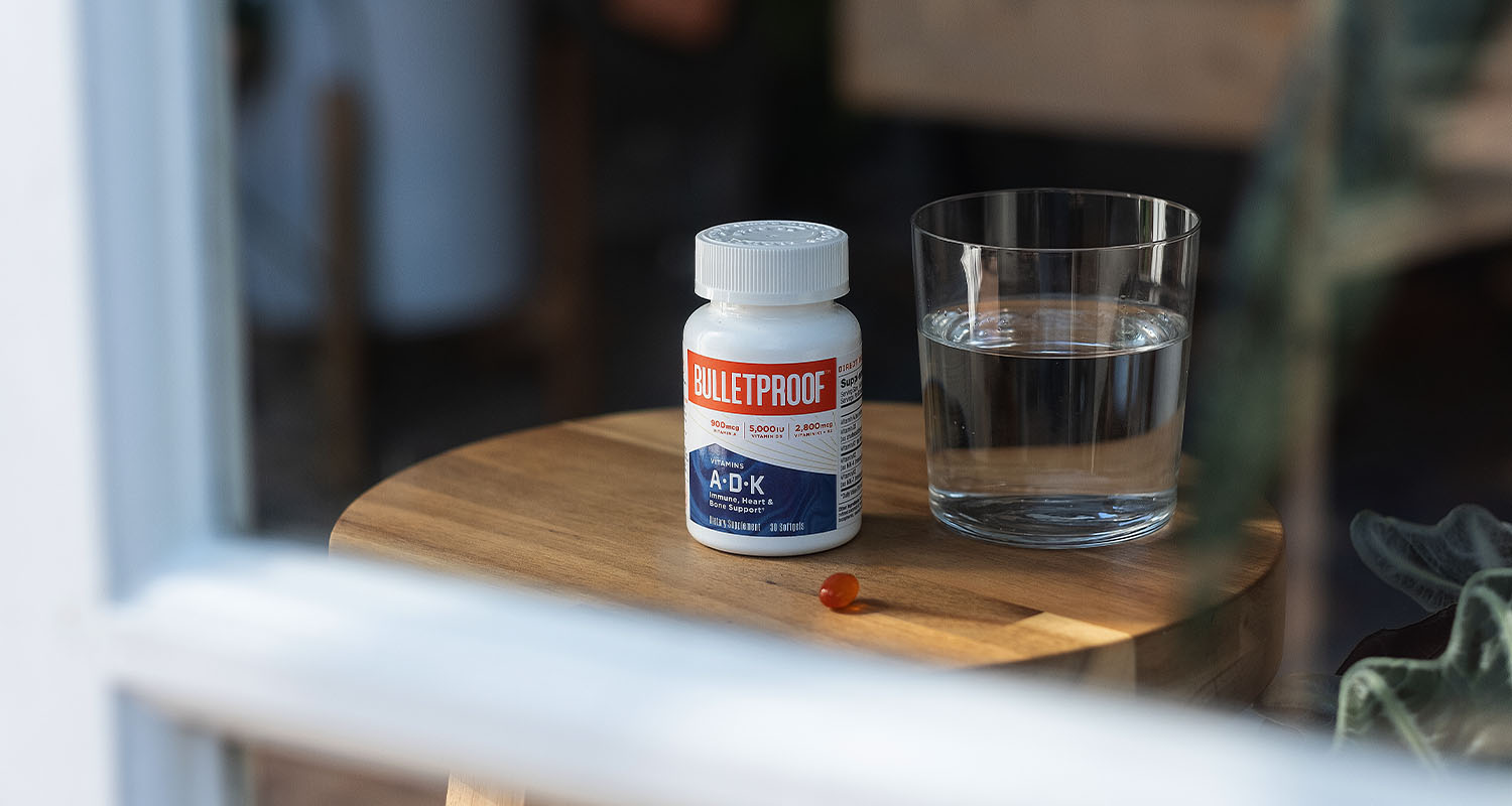 A bottle of Bulletproof Vitamins A-D-K next to a glass of water