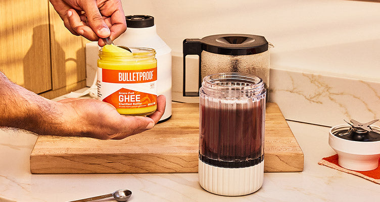 Hands scooping Bulletproof grass-fed ghee out of jar next to a cup of coffee