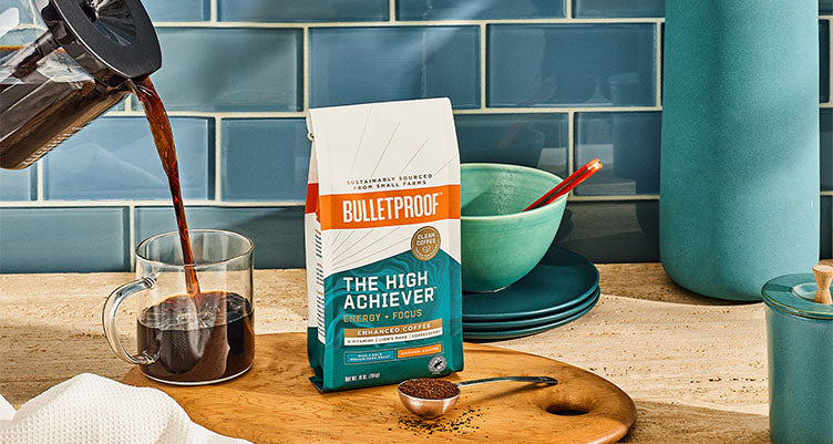 A bag of Bulletproof High Achiever coffee next to coffee being poured from a french press into a glass mug