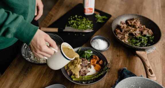 Person pouring sauce on plate full of meat and veggies