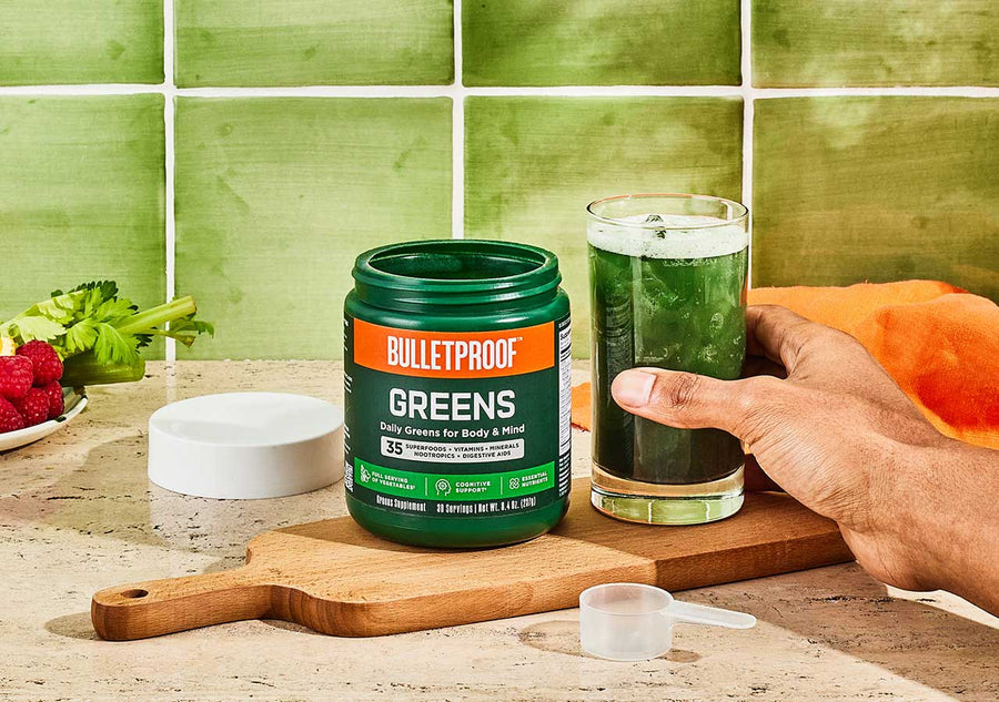 Bulletproof Greens open container beside a green drink with a hand holding it