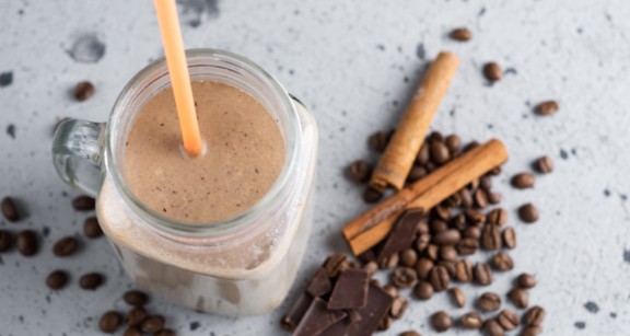 A mason jar of a coffee smoothie with cinnamon sticks