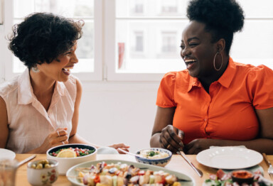 two women laughing while enjoying a meal together