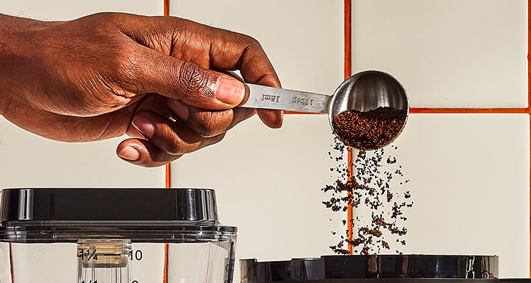 close up of someones hand dumping coffee grounds into the coffee maker