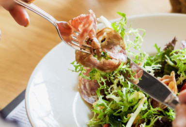 Person eating a salad with meat and shaved vegetable